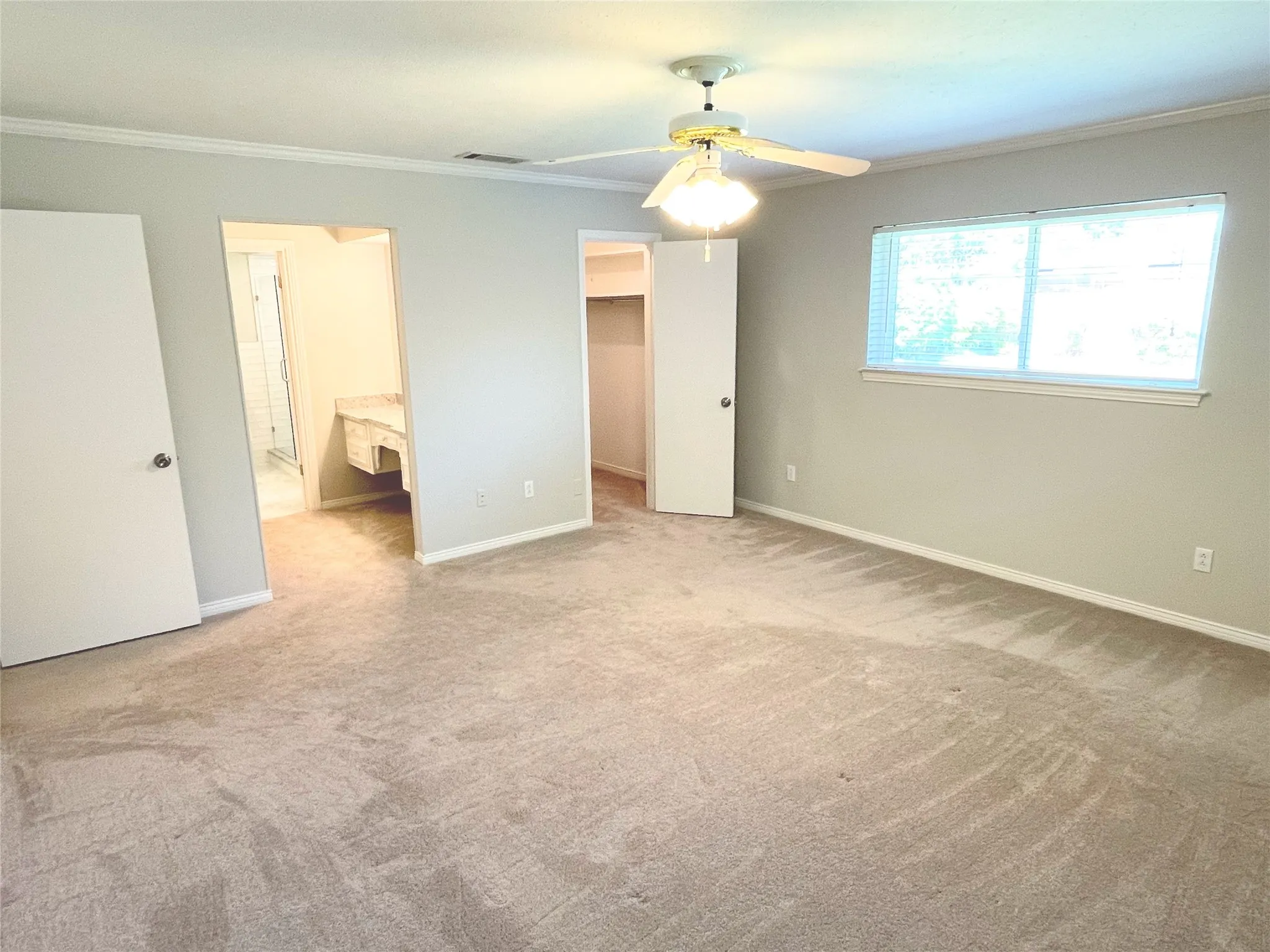 Primary bedroom with ceiling fan, light colored carpet, connected bathroom, and a spacious closet