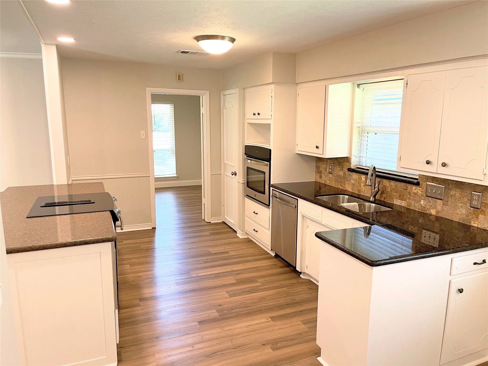 Kitchen with light hardwood / wood-style floors, white cabinetry, backsplash, stainless steel appliances, and sink