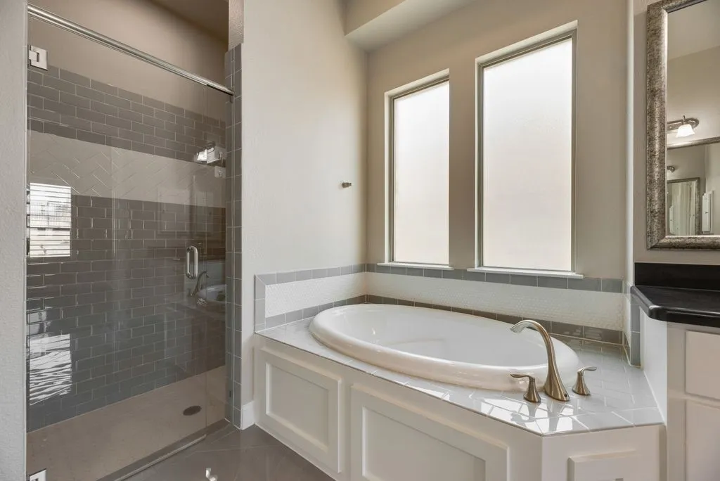Glass-enclosed shower with subway tile, integrated soaking tub, dual frosted windows, and a built-in vanity with a dark countertop