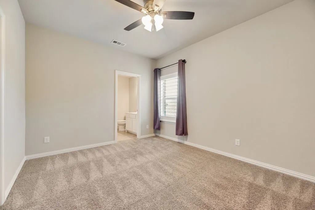Vaulted ceiling with a ceiling fan, carpeted flooring, window with blinds, and an attached bathroom featuring a vanity with a white cabinet
