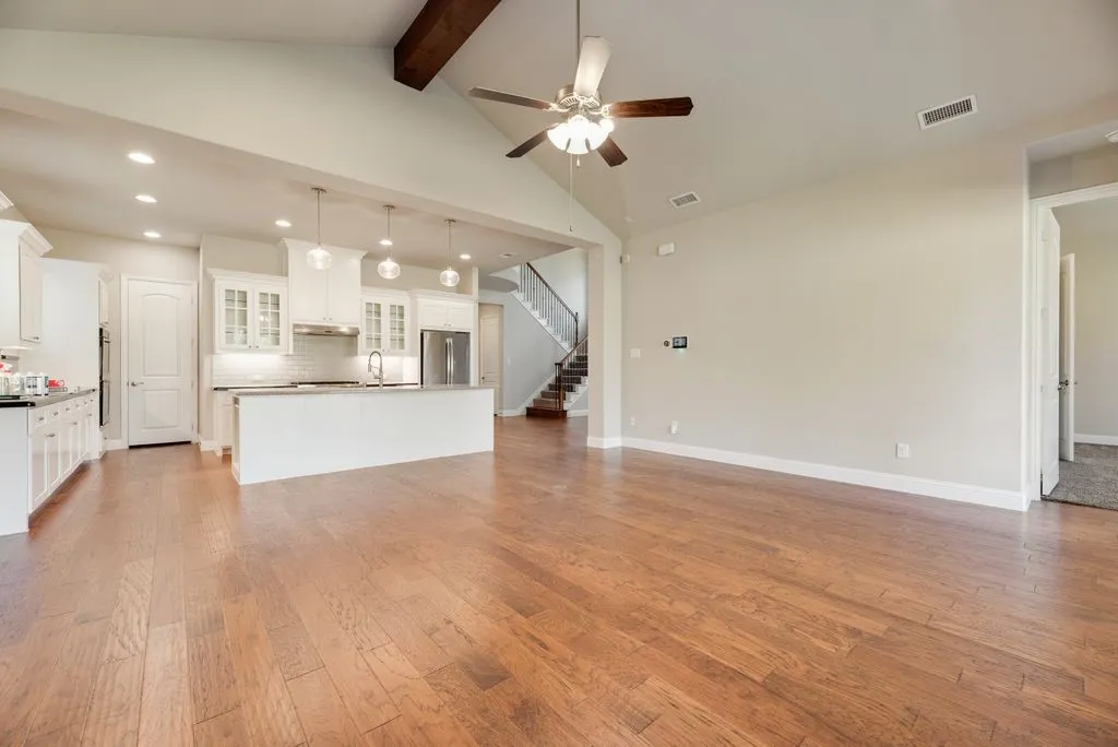 Expansive living area featuring wood-finish flooring, vaulted ceilings with a wood beam, and a ceiling fan