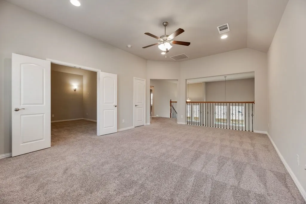 Vaulted ceiling, recessed lighting, ceiling fan, carpeted flooring, and a wrought iron and wood baluster railing