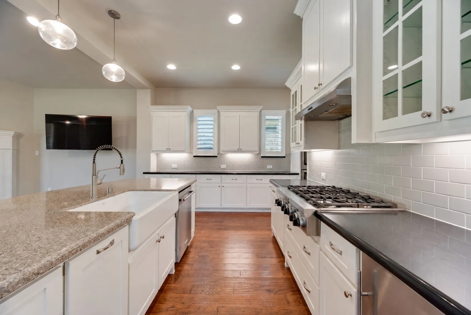 Spacious kitchen featuring an expansive island with a farmhouse sink and granite countertop, white shaker cabinetry, stainless steel appliances, and wood-finish flooring