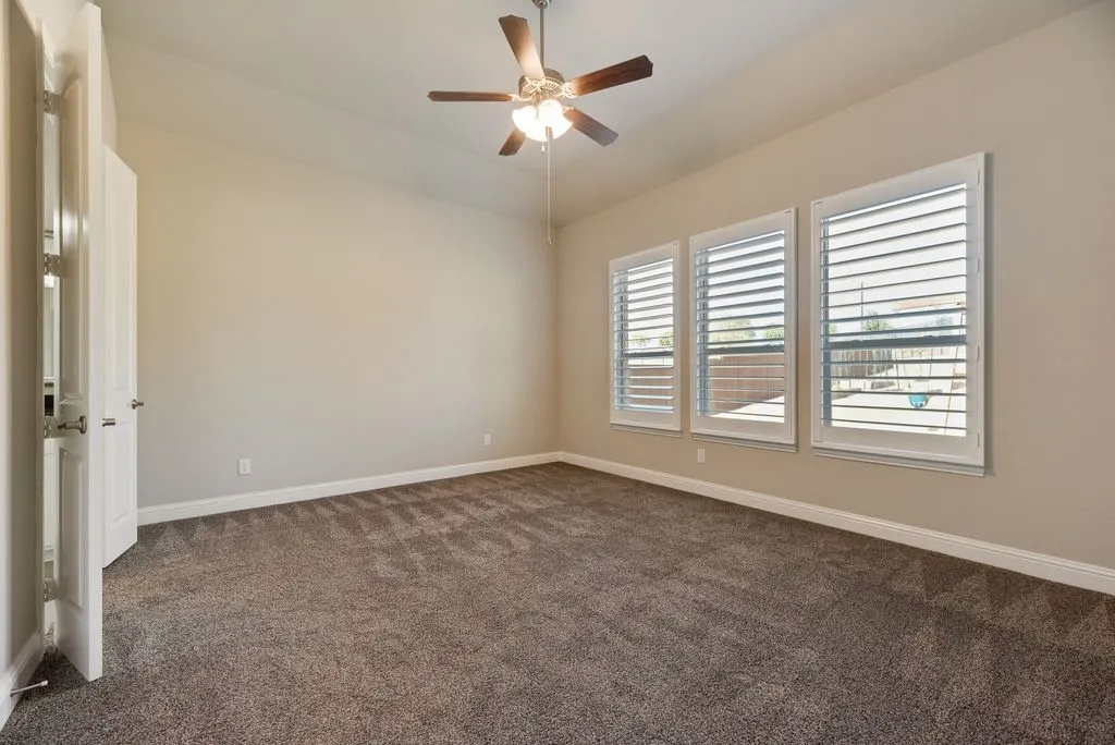 Vaulted ceiling with a ceiling fan and light fixture, three windows with plantation shutters, neutral-toned carpet, and a white paneled door
