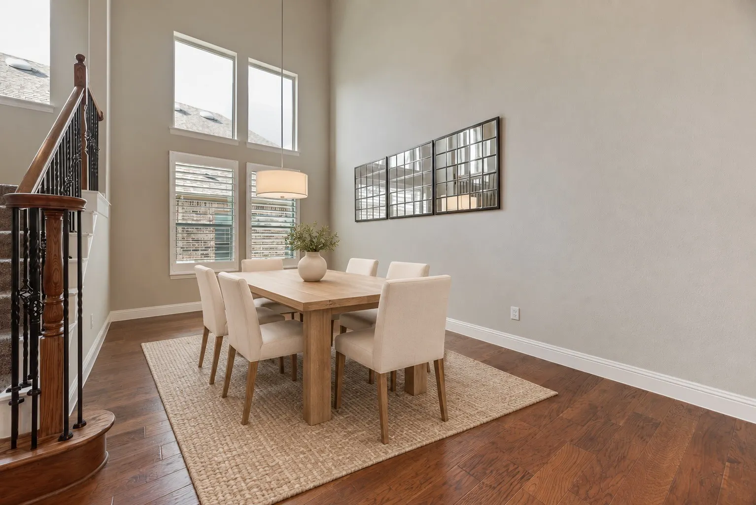Two-story dining space with high ceilings, wood-finish flooring, and multiple windows with plantation shutters