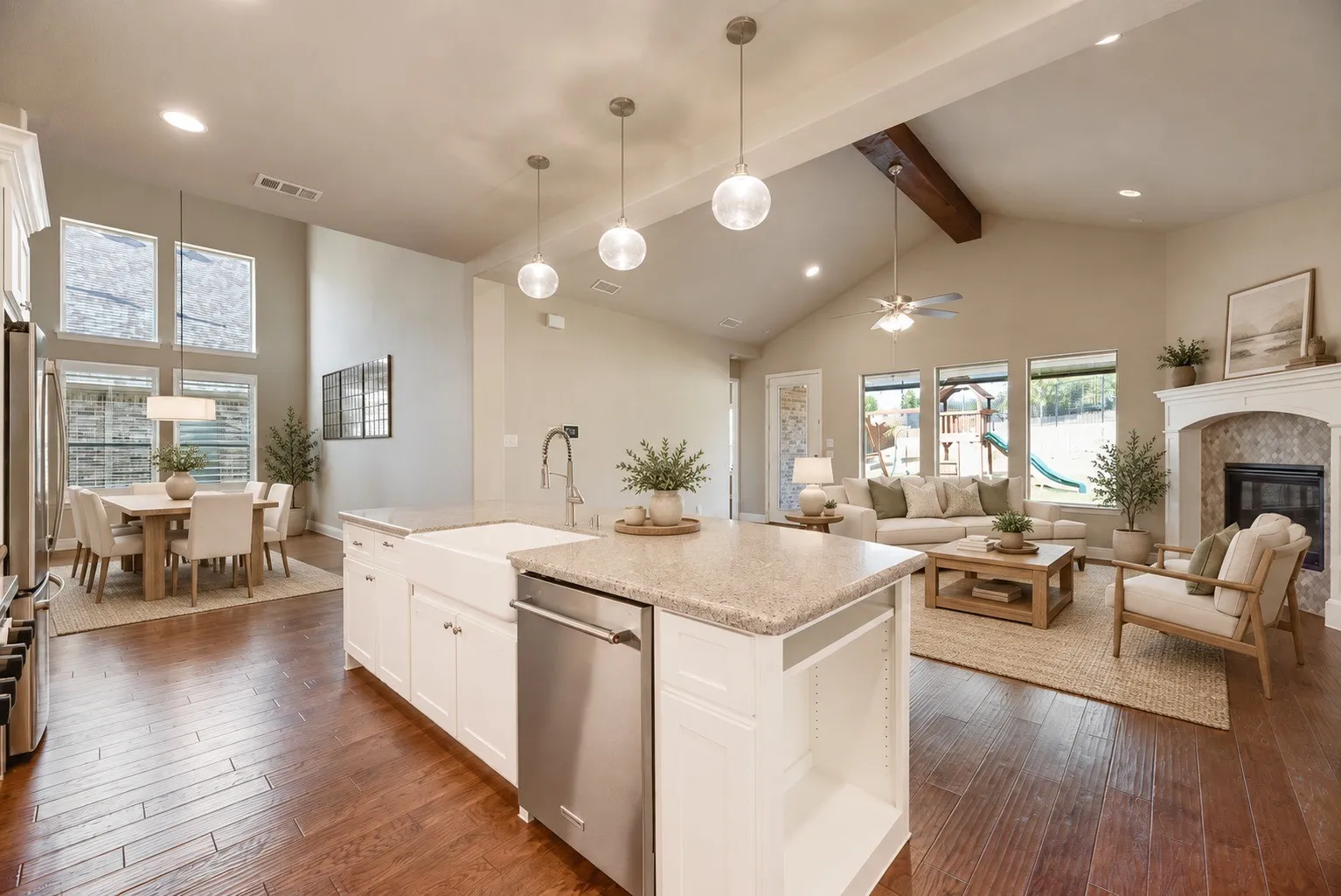 Open-concept living area featuring wood-finish flooring, vaulted ceilings with exposed beam, a stone-surround fireplace, and a kitchen island with a farmhouse sink