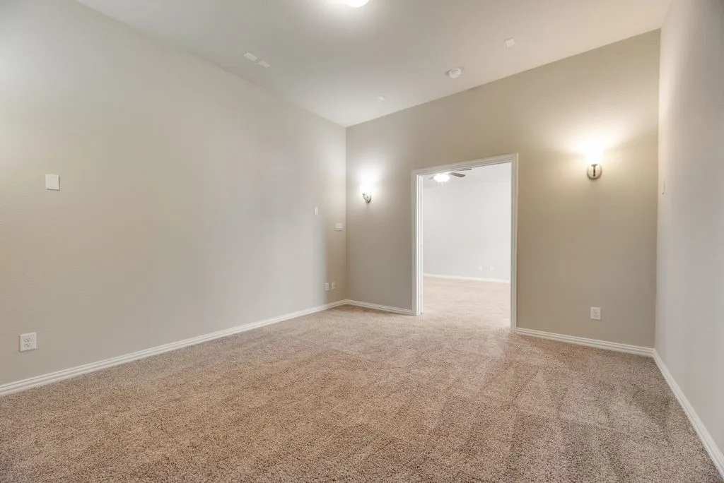 Neutral-toned carpet flooring, recessed ceiling lighting, wall-mounted sconce lighting, and a broad entryway