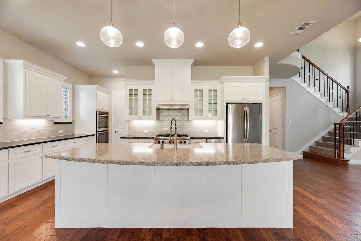 Open-concept kitchen with a large island, stainless steel appliances, white cabinetry, and wood-finish flooring