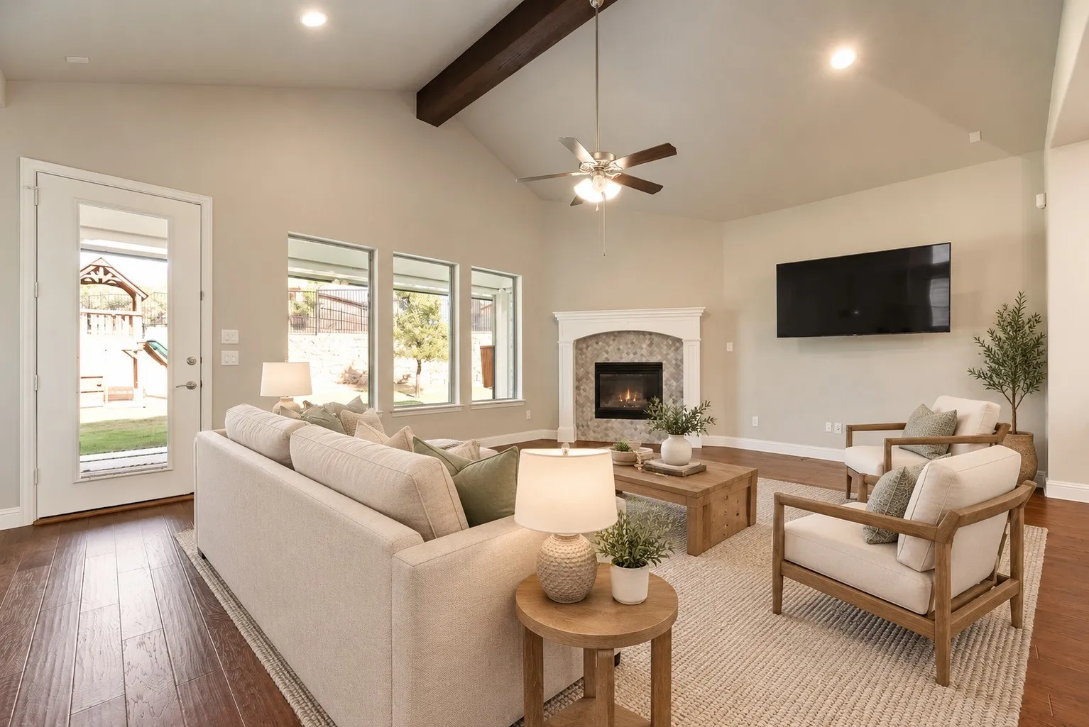 Vaulted ceilings featuring an exposed beam, a stone-faced fireplace with a mantel, dark wood-finish flooring, and multiple windows