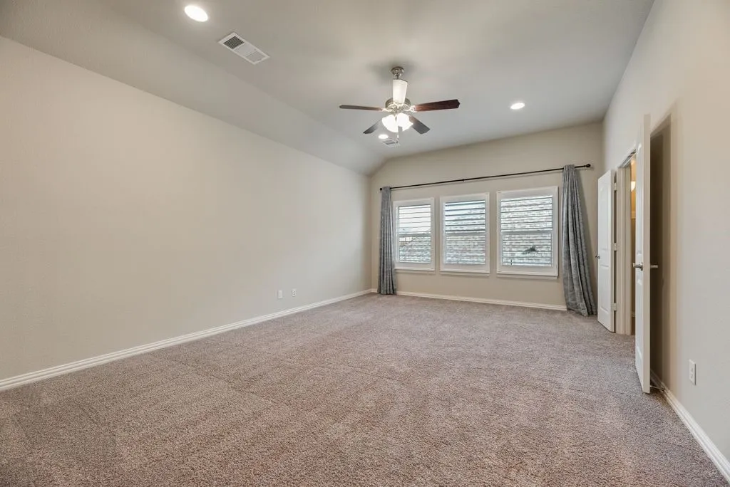 Spacious room with vaulted ceiling, recessed lighting, ceiling fan, three large windows, and neutral carpeting