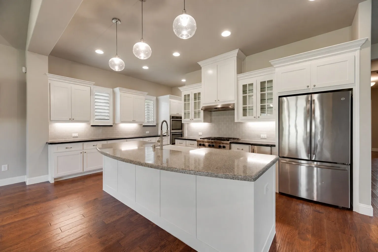 Spacious kitchen featuring an expansive center island with a sink, white cabinetry, integrated stainless steel appliances, pendant lighting, and wood-finish flooring