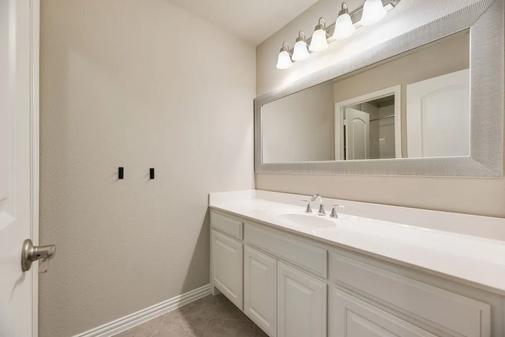Vanity with integrated sink, chrome faucet, white cabinetry, and a large framed mirror with overhead lighting