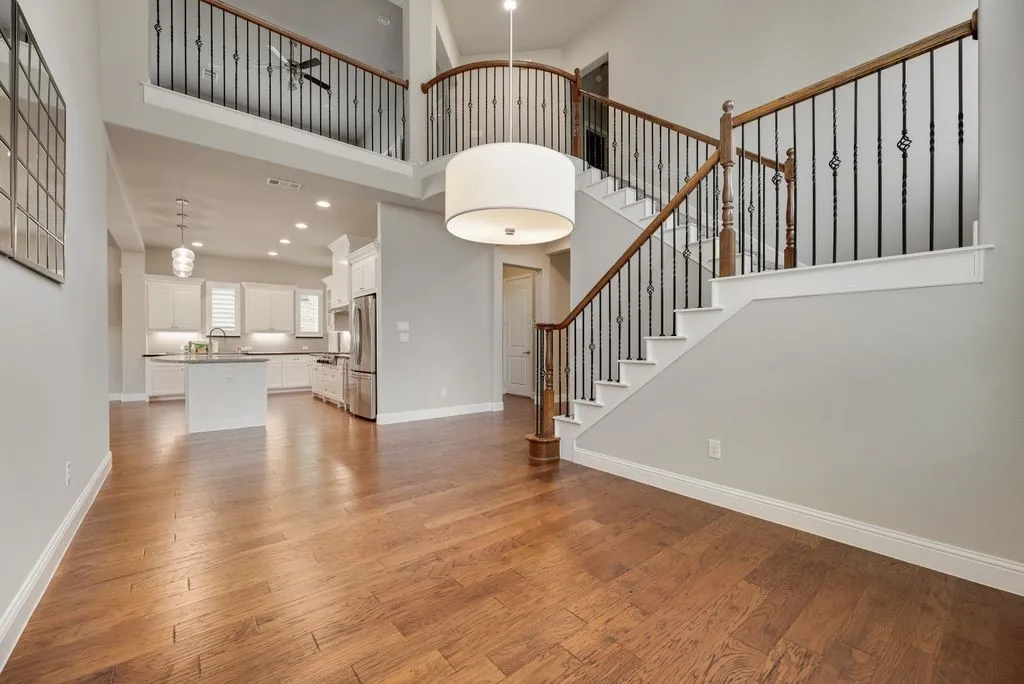 Wood-finish flooring throughout, wrought iron and wood staircase, upper-level balcony, suspended drum light fixture, and recessed lighting