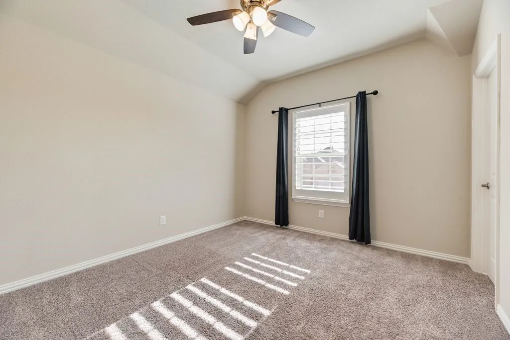 Vaulted ceiling with a ceiling fan, window with plantation shutters, light-colored walls, and textured carpeting