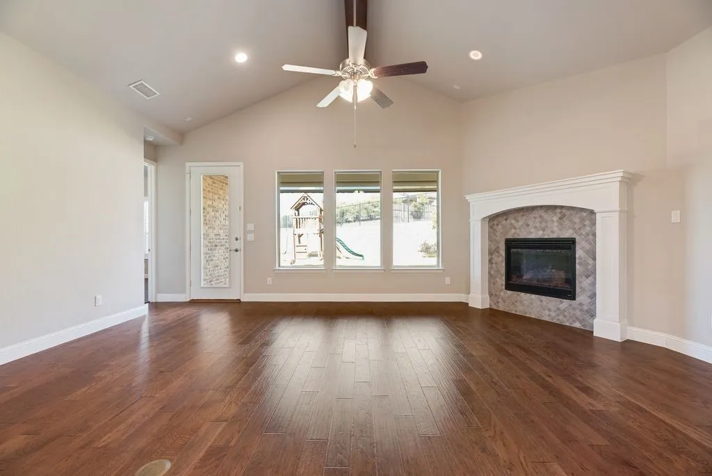 Vaulted ceilings with recessed lighting, wood-finish flooring, and a fireplace with a decorative mantel and tile surround