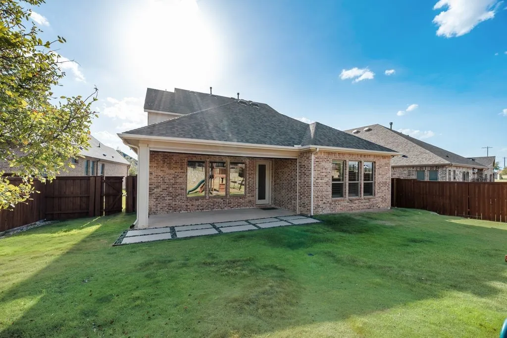 Expansive backyard featuring a manicured lawn, brick exterior, covered patio, and privacy fencing