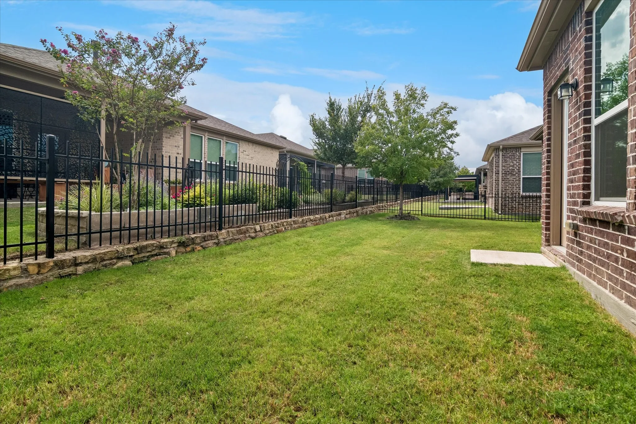 Expansive green lawn with a black wrought iron fence and a stone retaining wall