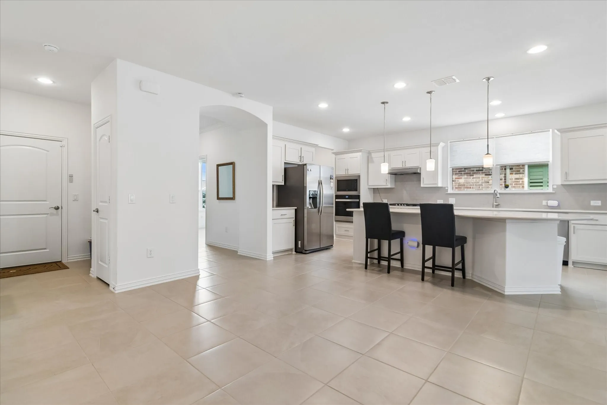 Open-concept layout featuring light-toned tile flooring, an arched entryway, and recessed lighting