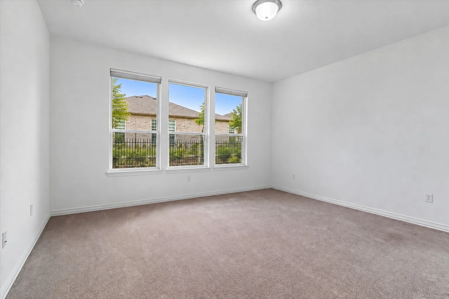 Neutral wall color, wall-to-wall carpeting, three multi-pane windows, and a flush-mount ceiling light fixture