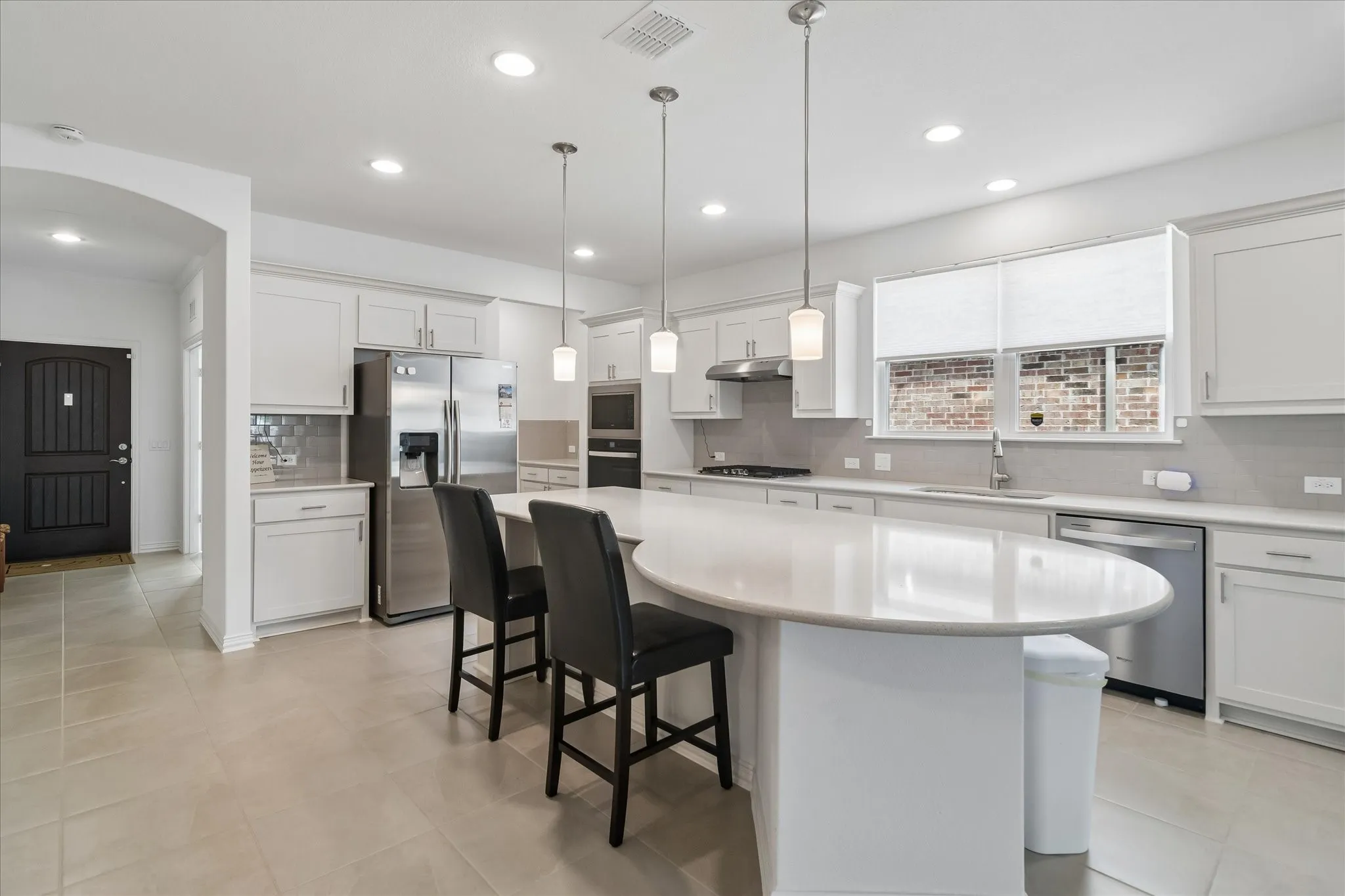 Expansive kitchen featuring an oval-shaped island with seating, recessed and pendant lighting, white cabinetry, stainless steel appliances, and a tiled backsplash