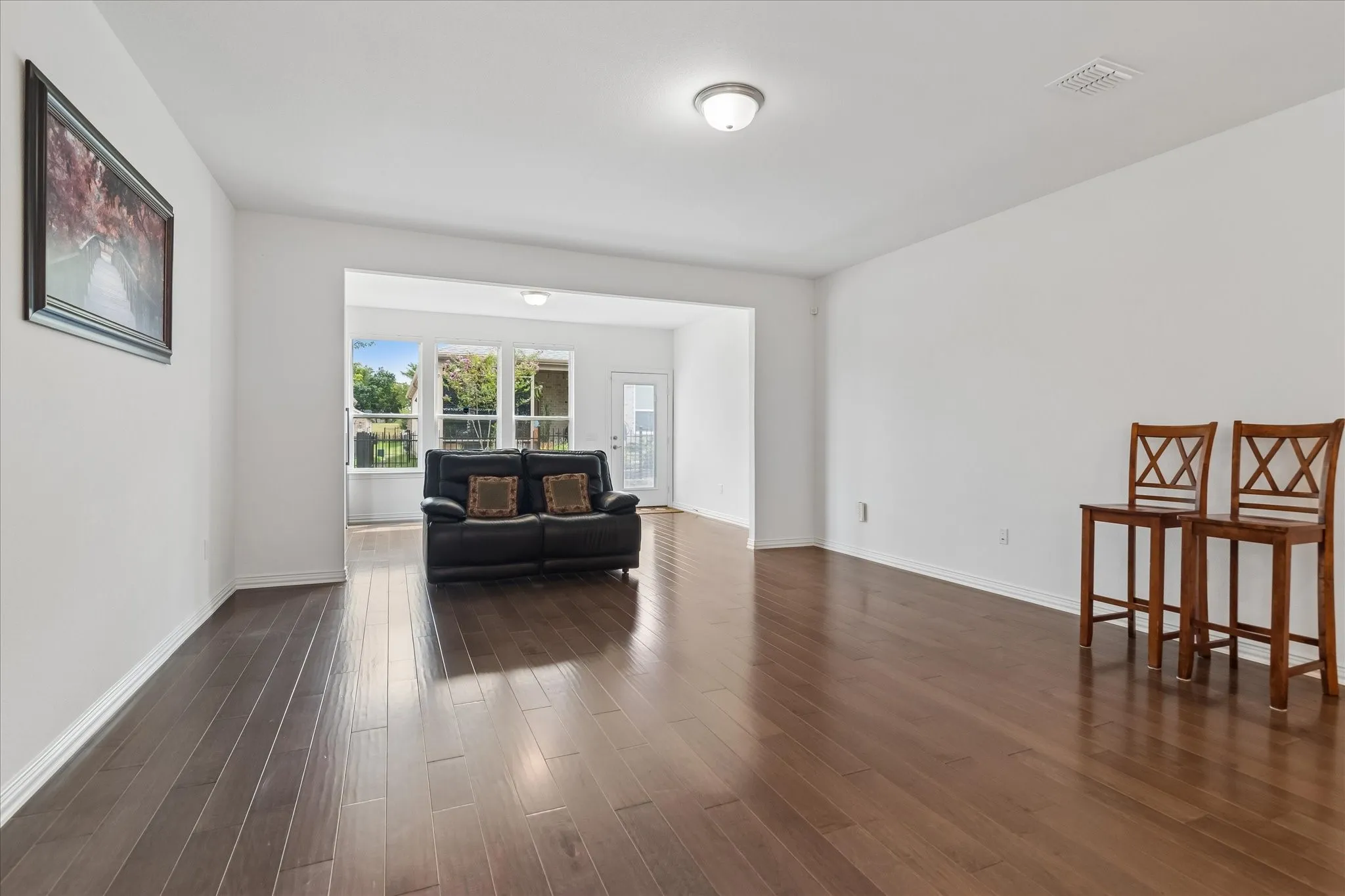 Wood-finish flooring throughout, white painted walls, recessed ceiling light, and large windows with exterior foliage