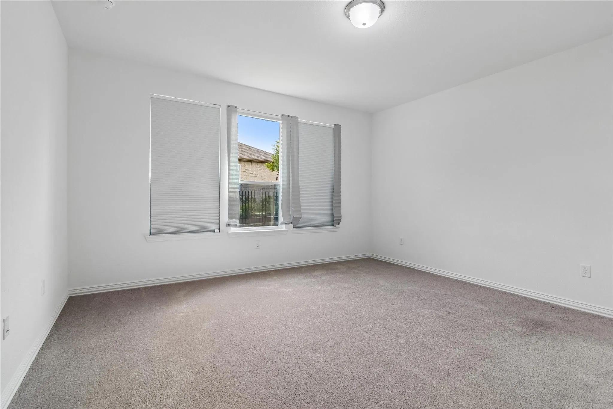 Spacious room featuring neutral carpet flooring, white painted walls, a large window with blinds, and a ceiling-mounted light fixture