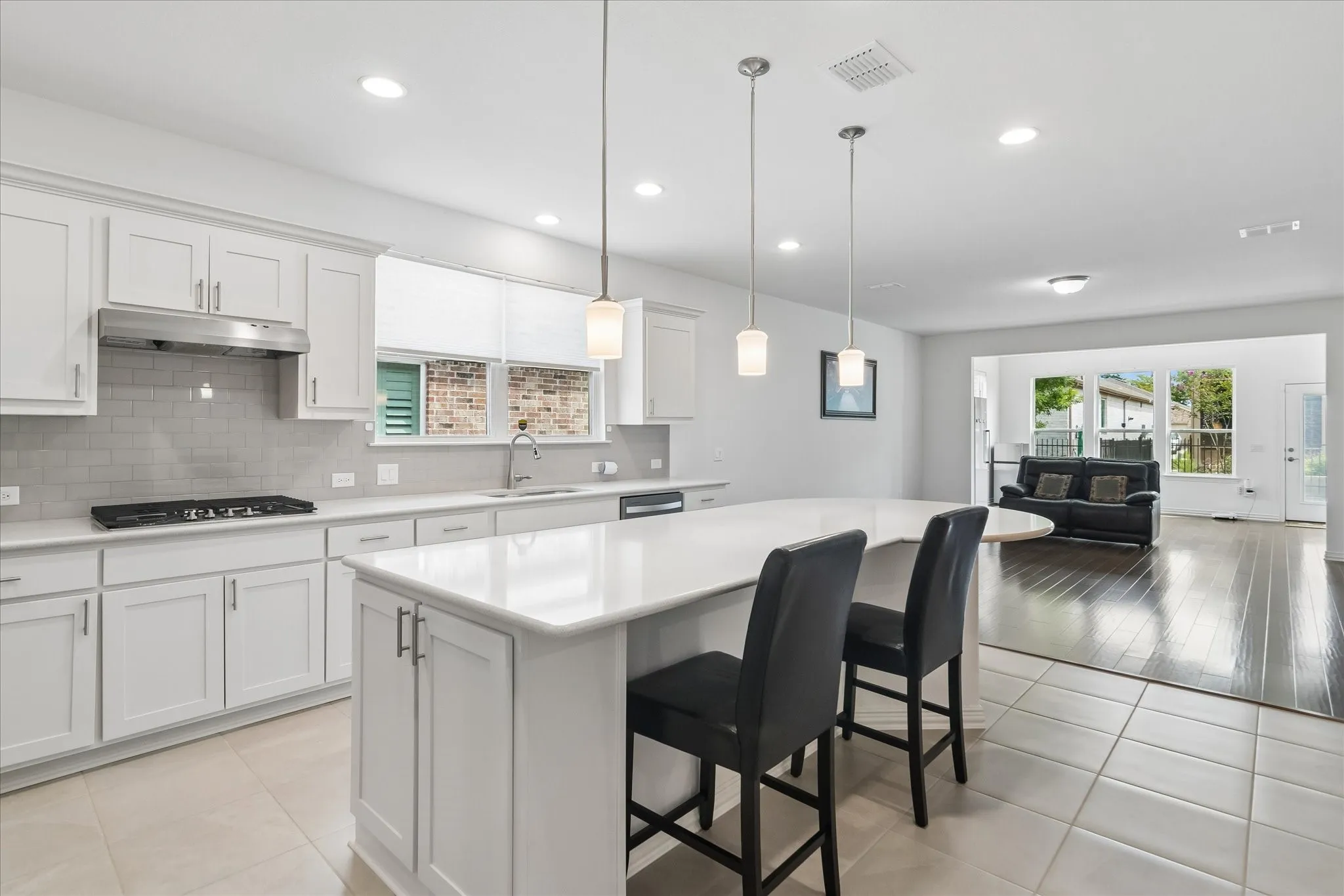 White cabinetry with brushed nickel hardware, light tile flooring, stainless steel range hood, stone countertops, and a white subway tile backsplash