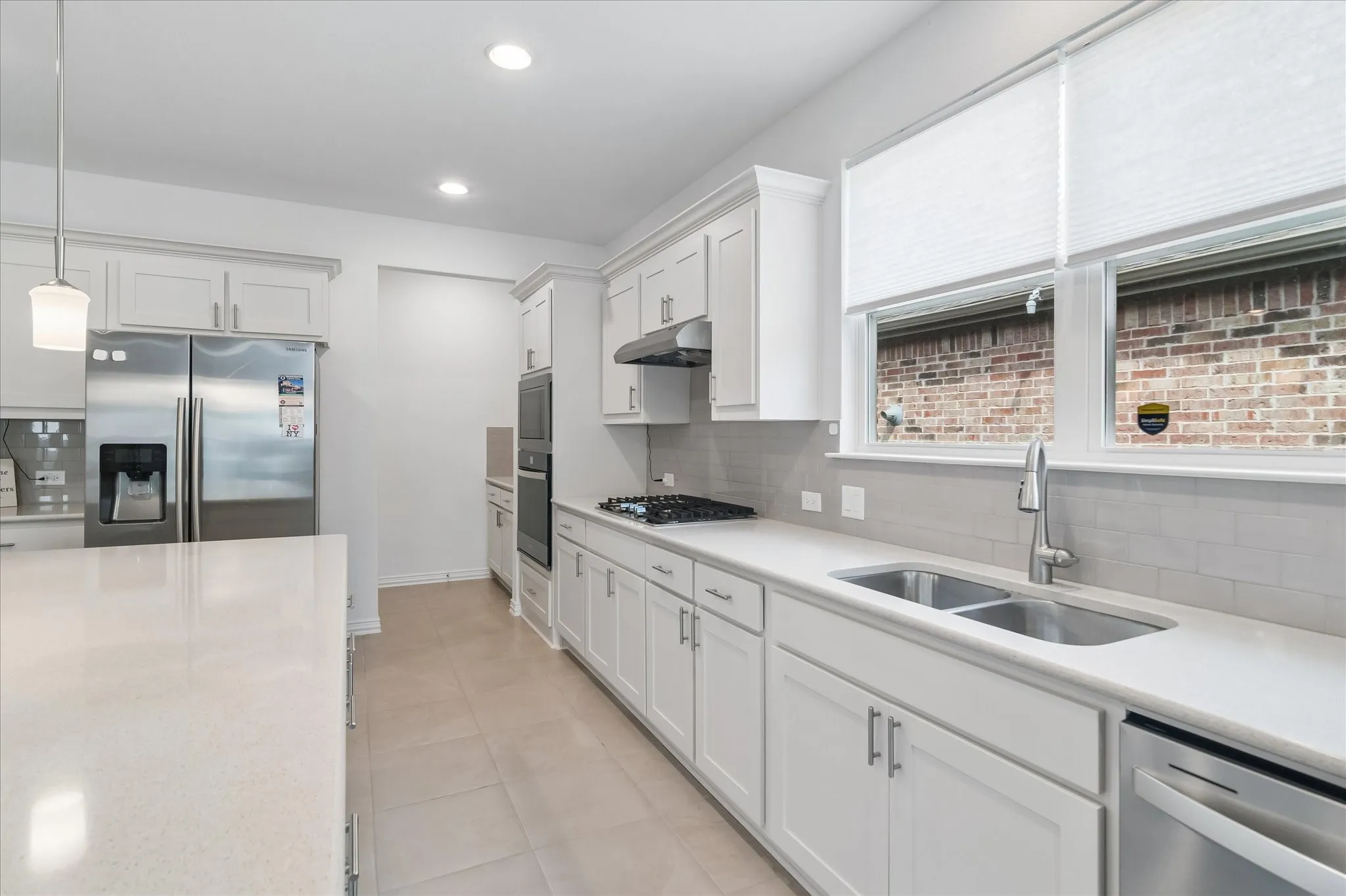 Modern kitchen featuring white cabinetry, light-toned countertops, stainless steel appliances, a double basin sink, and tile flooring