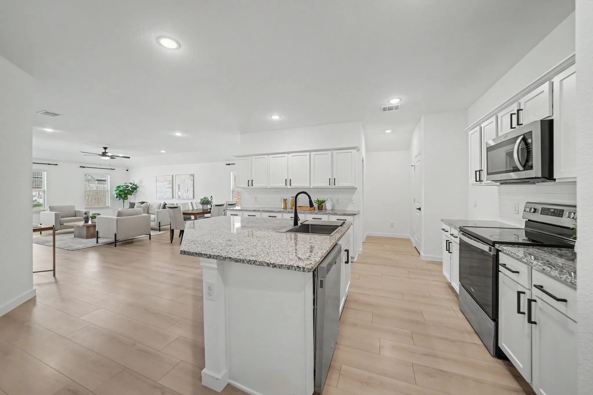 Open-concept kitchen with granite countertops, wood-finish flooring, white cabinetry, recessed lighting, and stainless steel appliances