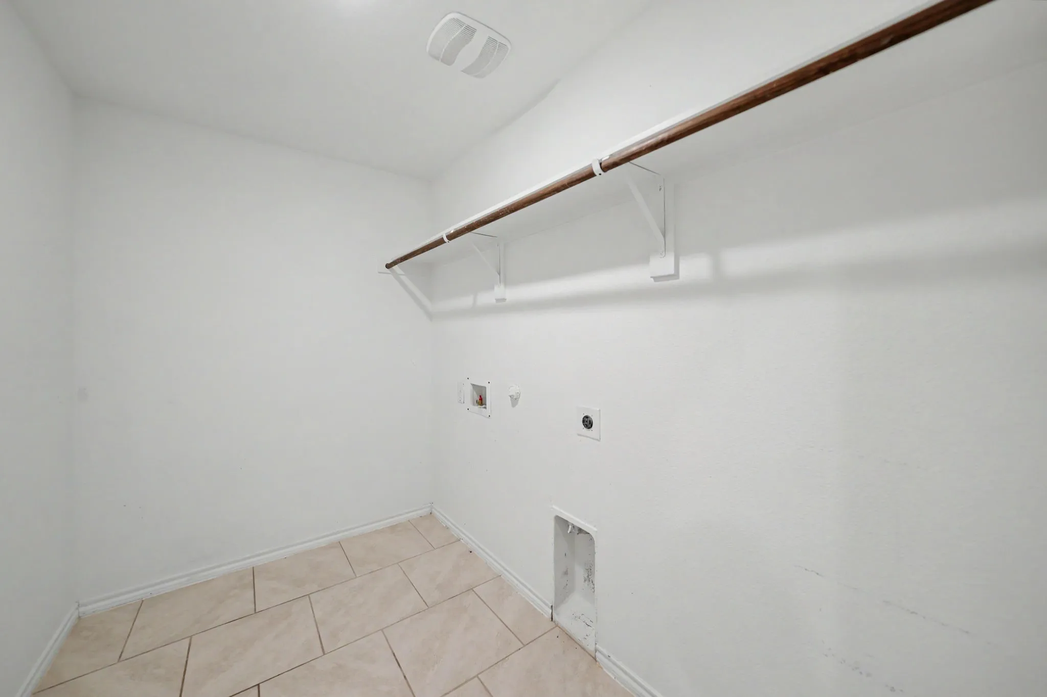 White walls with a wooden hanging rod, tile flooring, and utility hookups