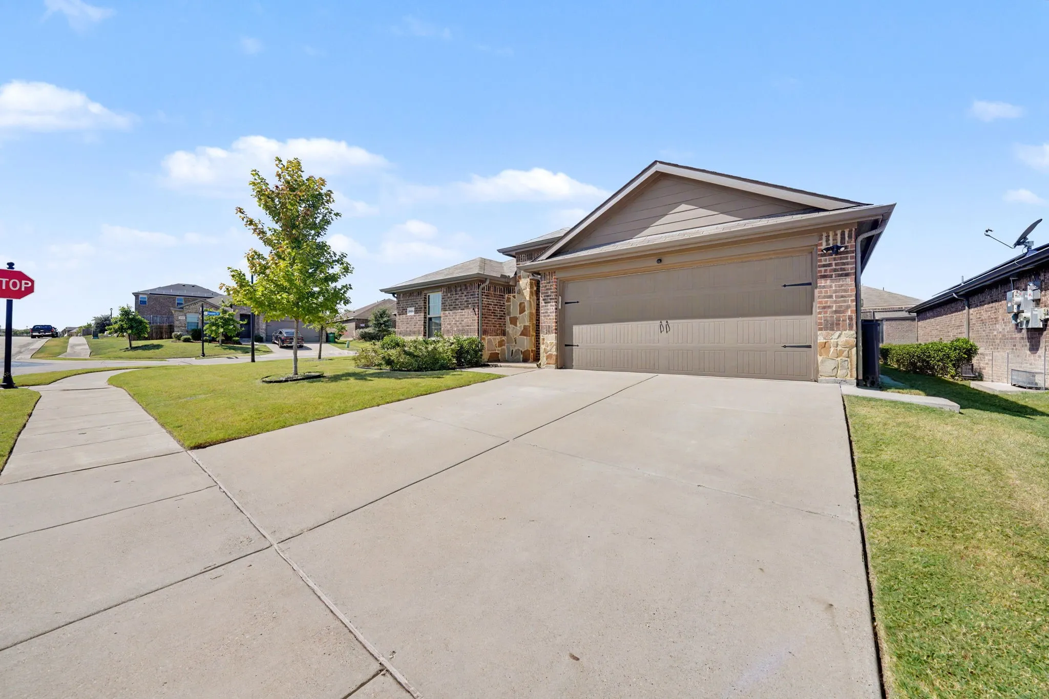 Brick and stone exterior with siding accents, attached garage, concrete driveway, and manicured lawn