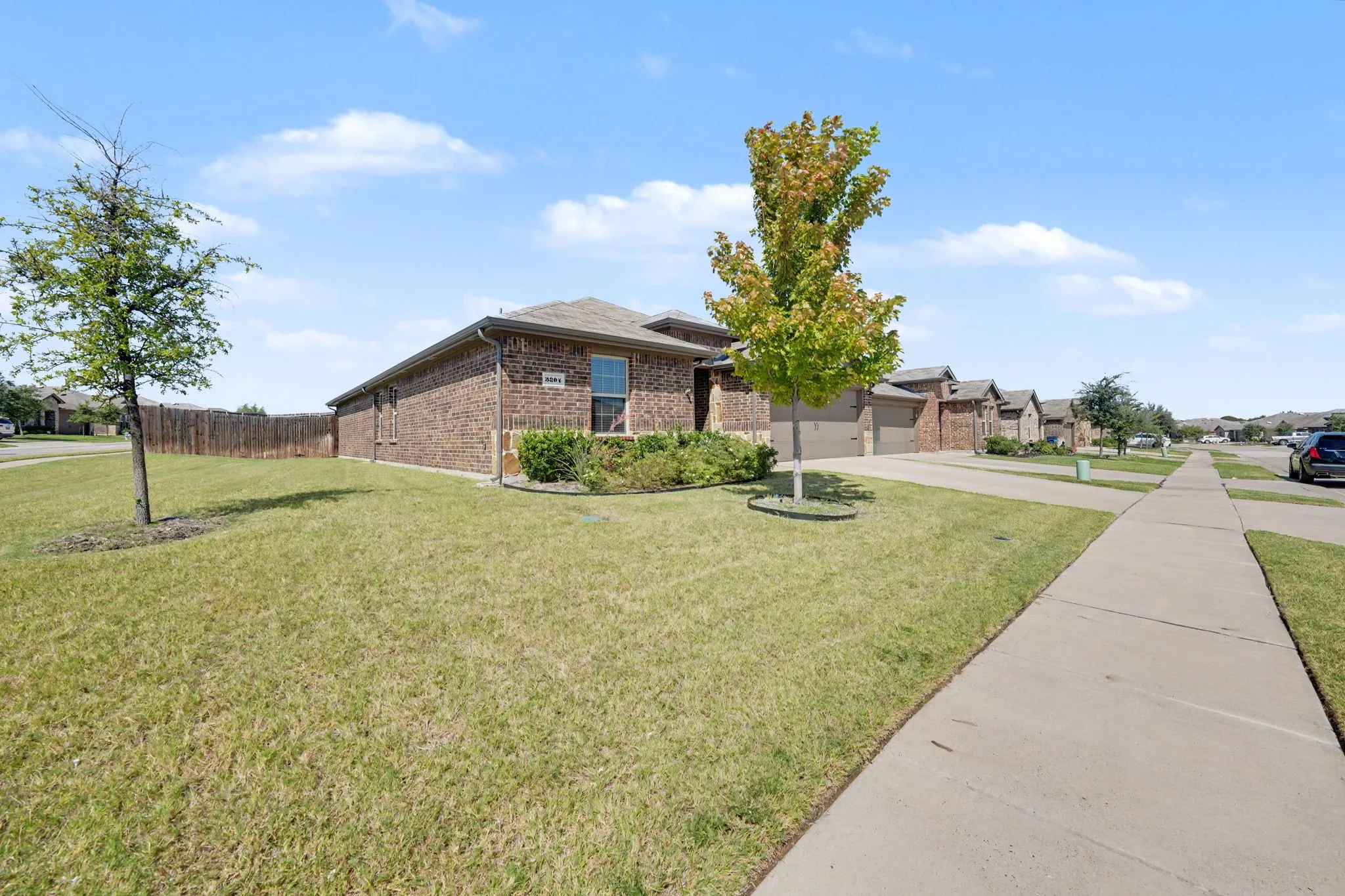 Brick exterior construction, multiple garage doors, concrete sidewalk, fenced backyard, mature trees