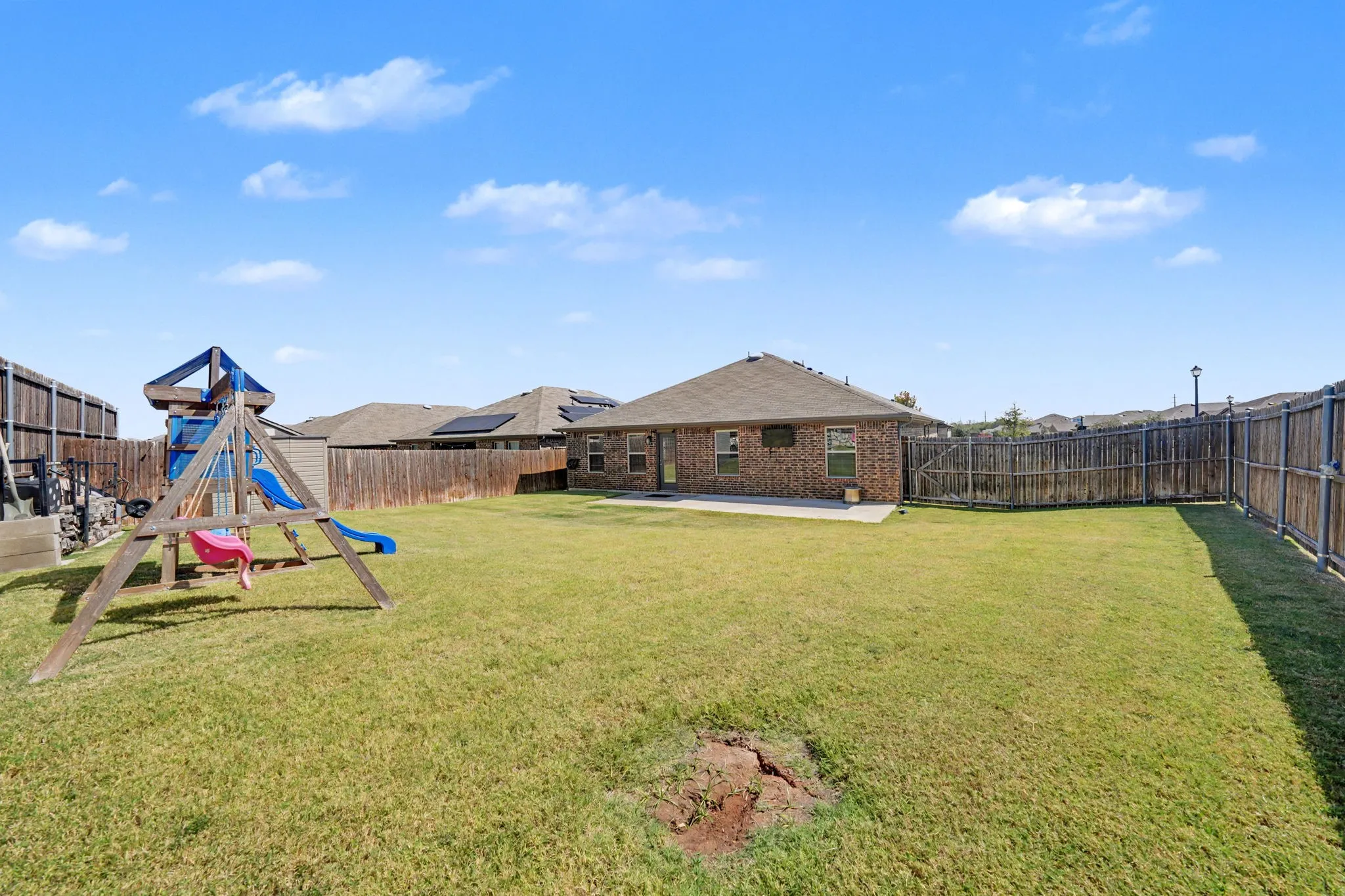 Expansive grassy yard with wood fencing, a concrete patio, and a brick exterior