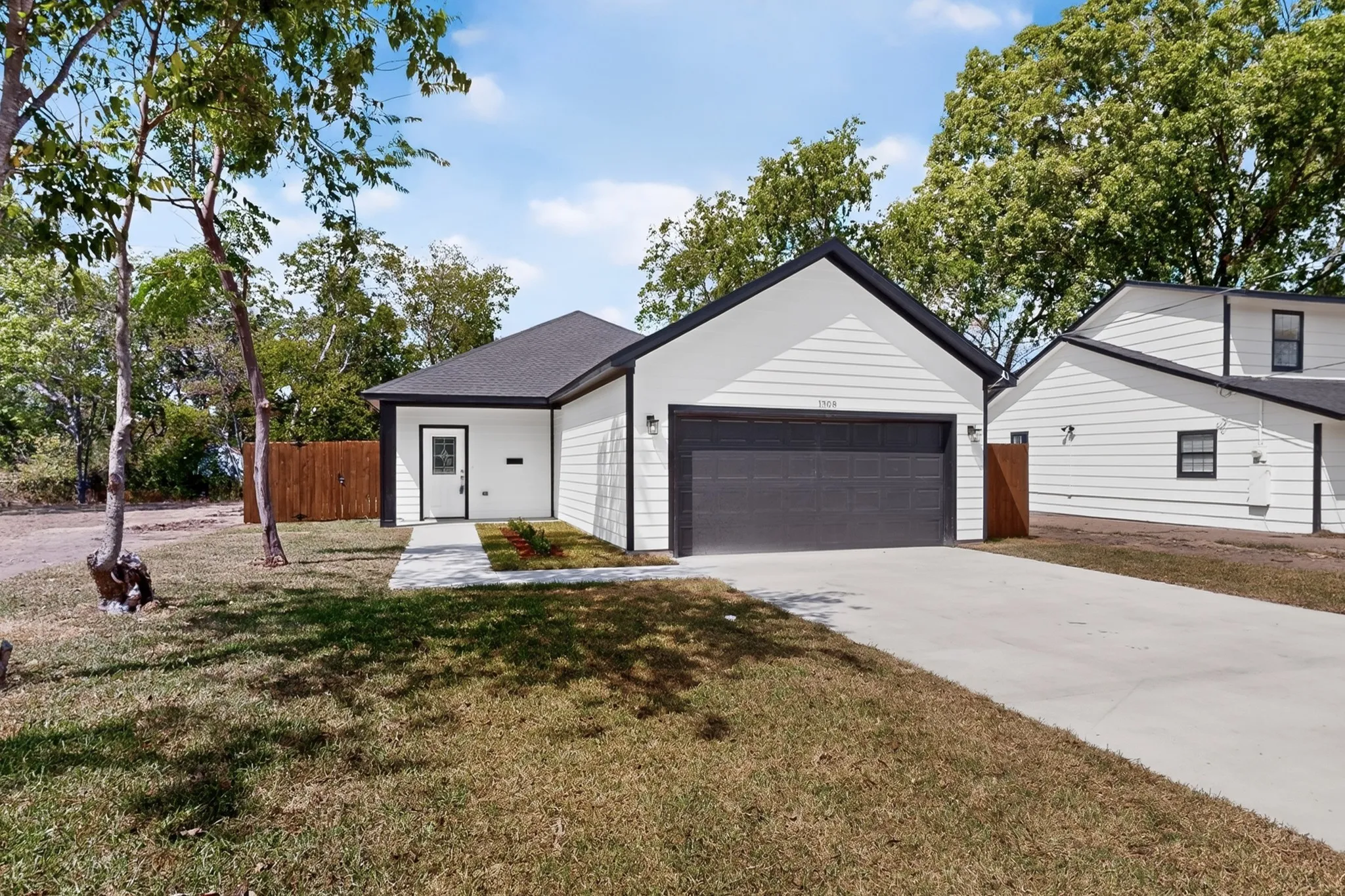 Modern white siding exterior with dark trim accents, a dark-colored garage door, a concrete driveway, and a paved walkway to the front entry