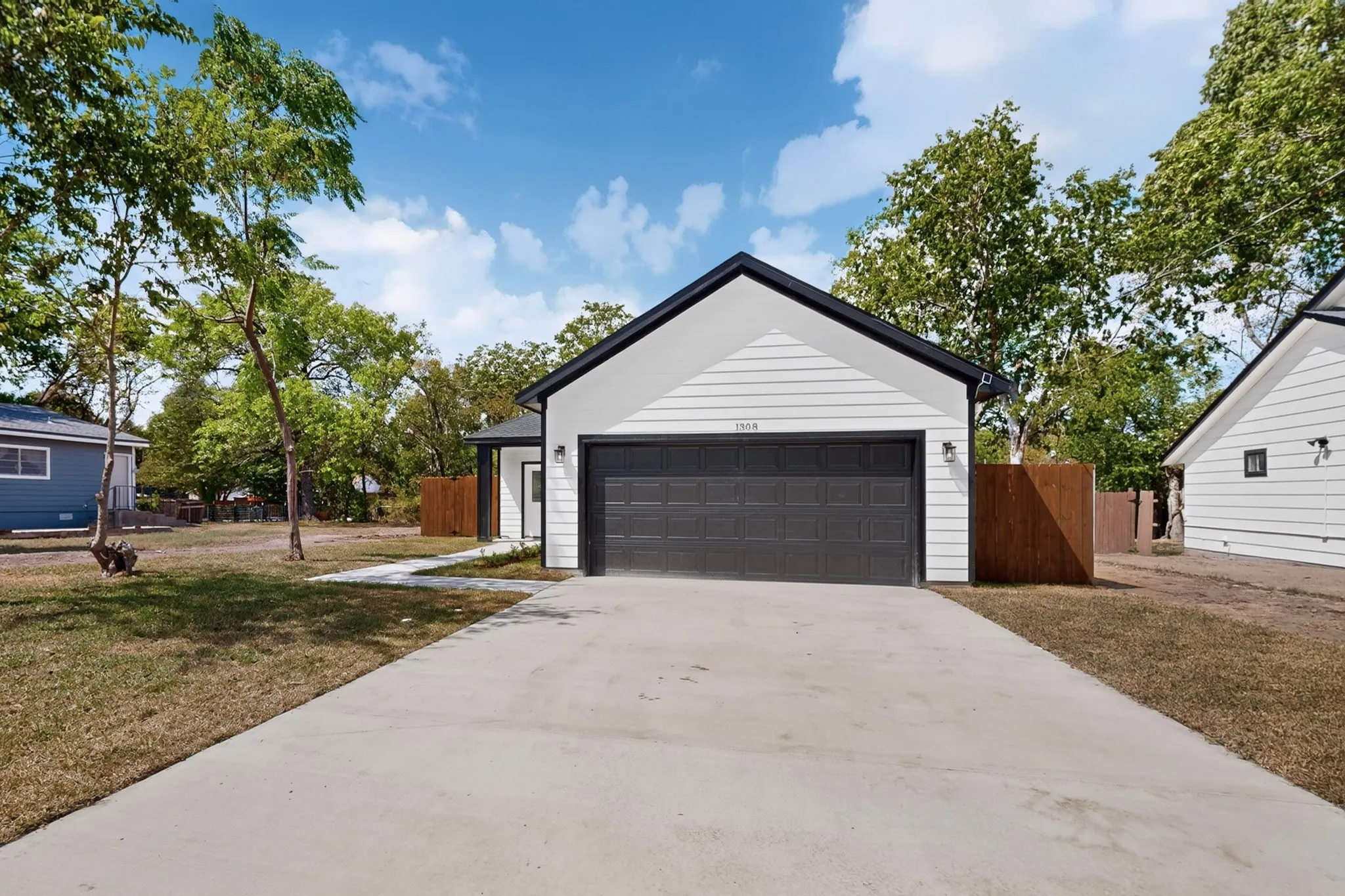 Contemporary white siding exterior with a black trim roof, attached dark gray garage door, concrete driveway, and a wooden privacy fence