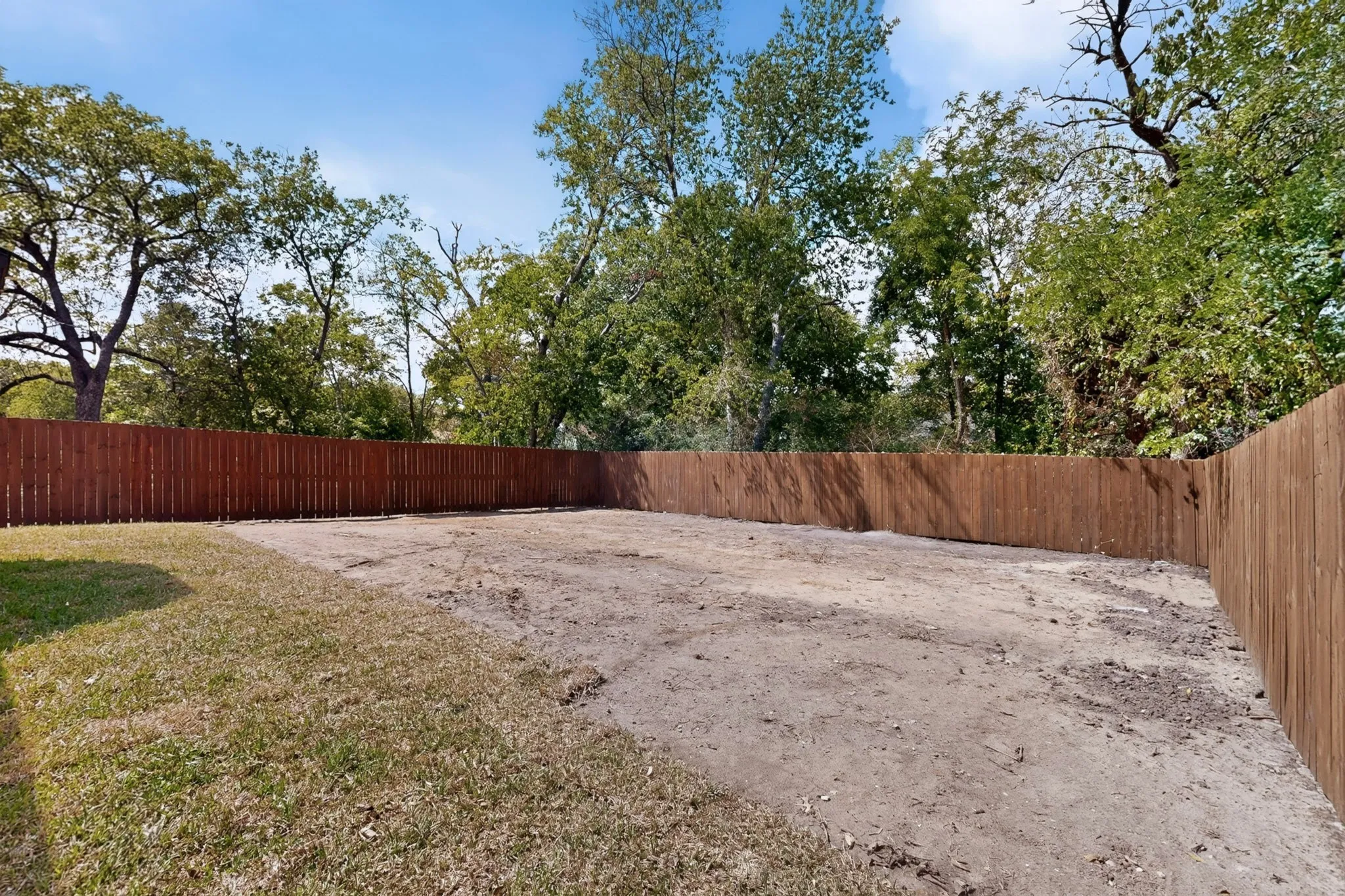 Expansive outdoor space featuring a wood privacy fence and mature trees.