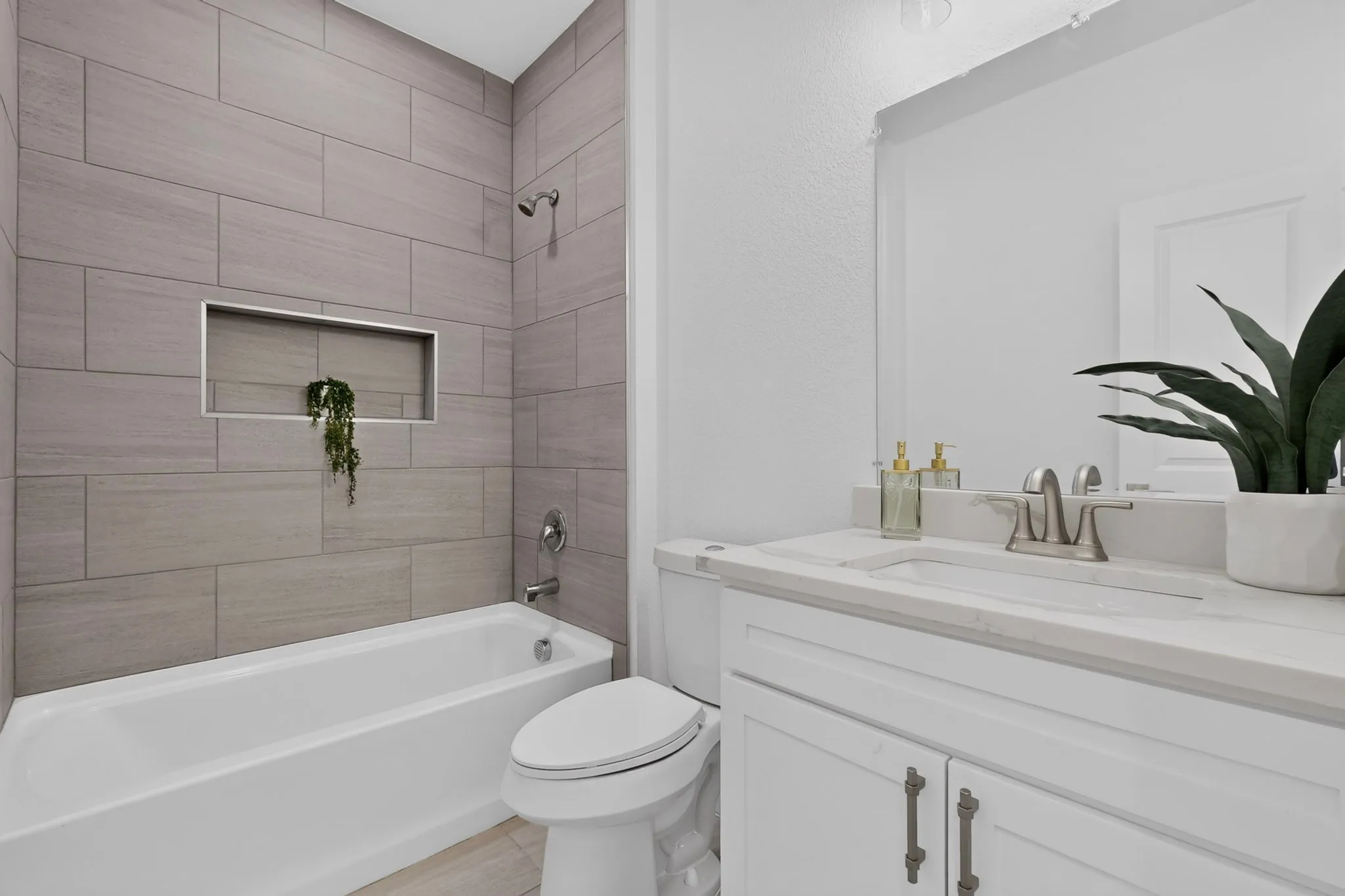 Tile-surround bathtub with a recessed niche, brushed nickel fixtures, a white vanity with panel-front cabinetry, and an integrated sink with a light-toned countertop