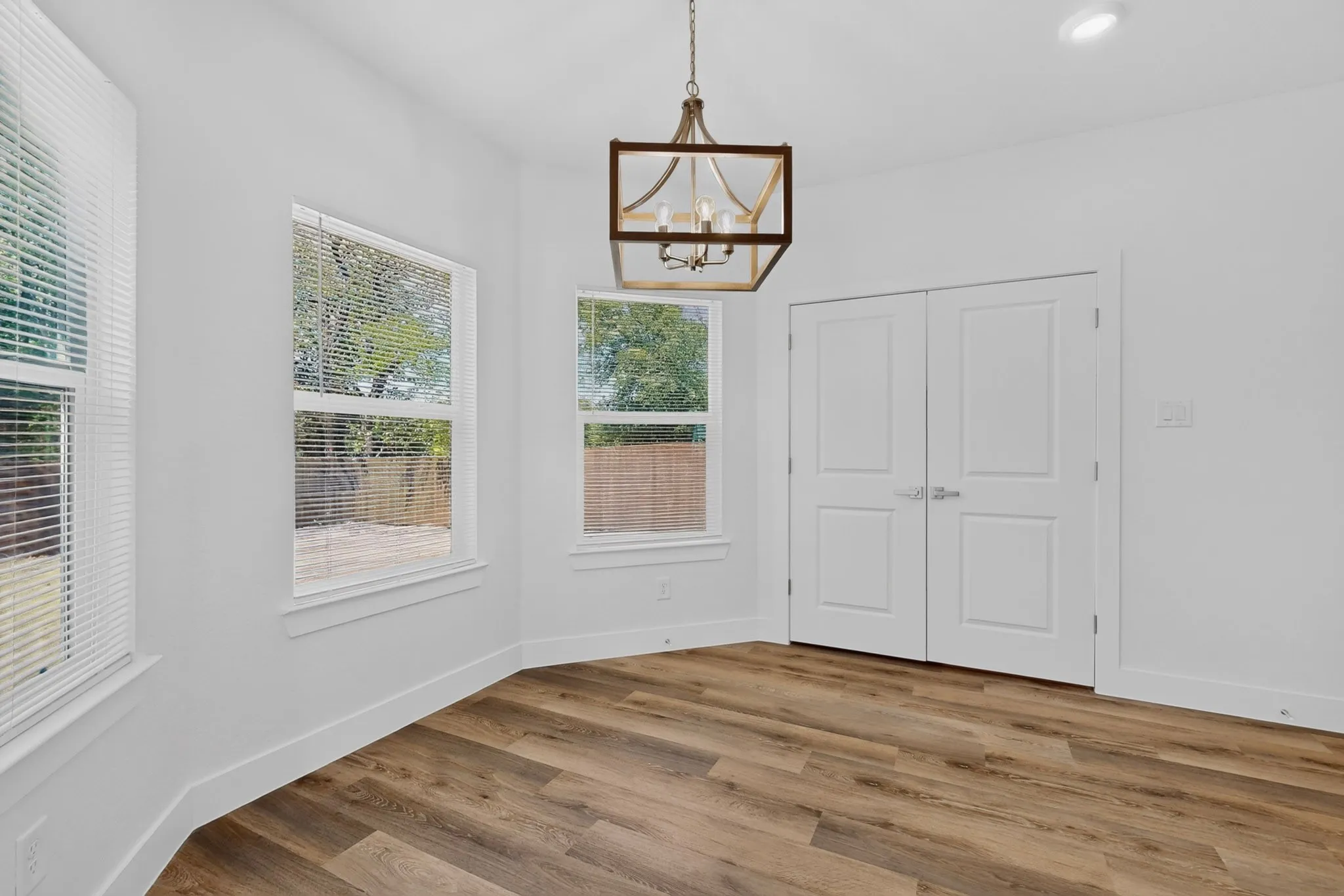 Wood-finish flooring with white baseboards, a contemporary chandelier, recessed ceiling lighting, and crisp white walls.