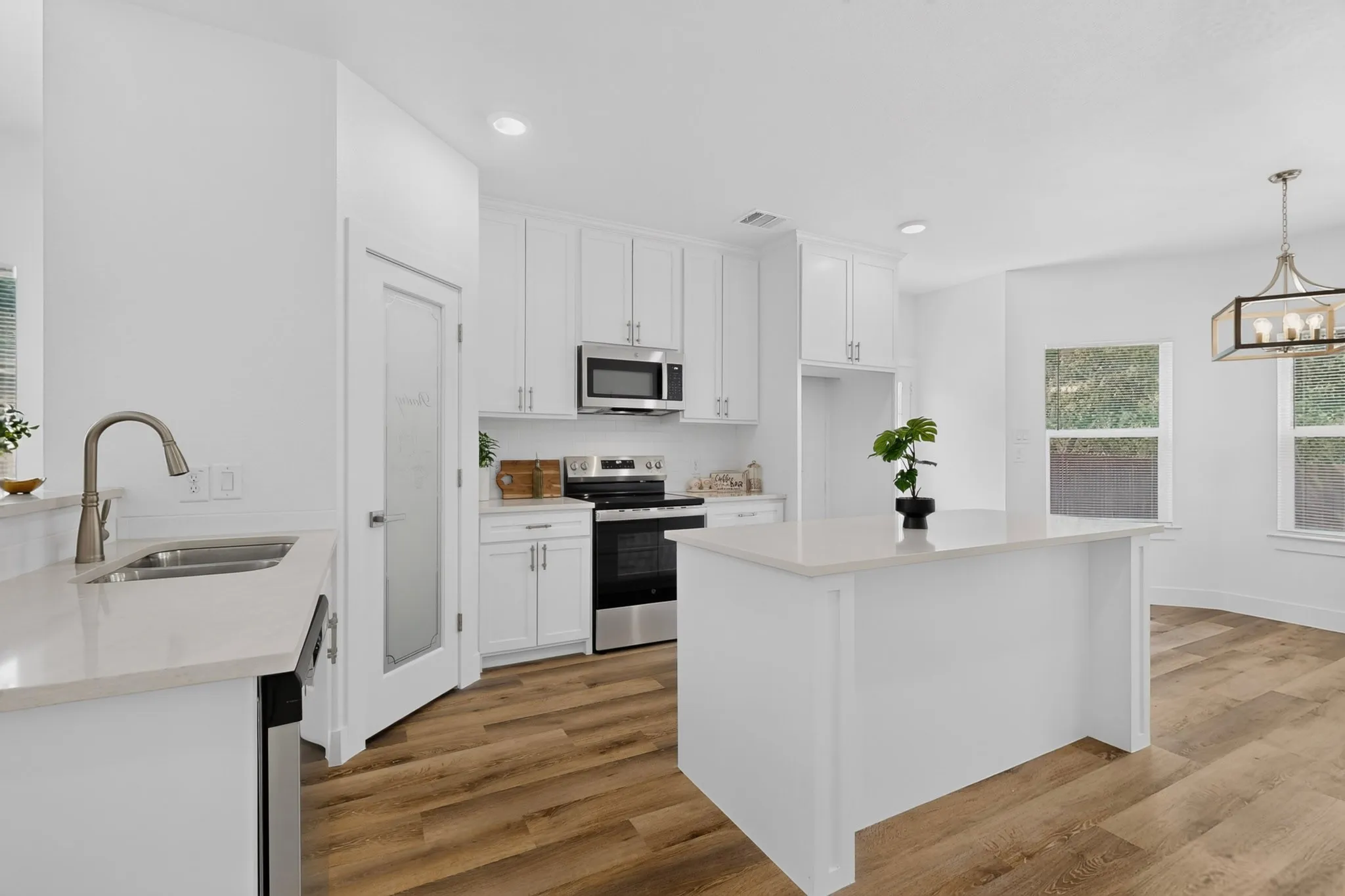 White cabinetry, stainless steel appliances, wood-finish flooring, recessed lighting, and a kitchen island with a light-colored countertop