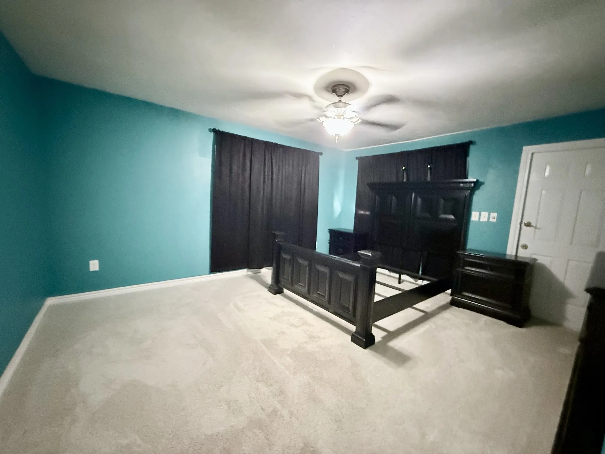 Plush carpeting, ceiling fan with light fixture, and a white door with hardware
