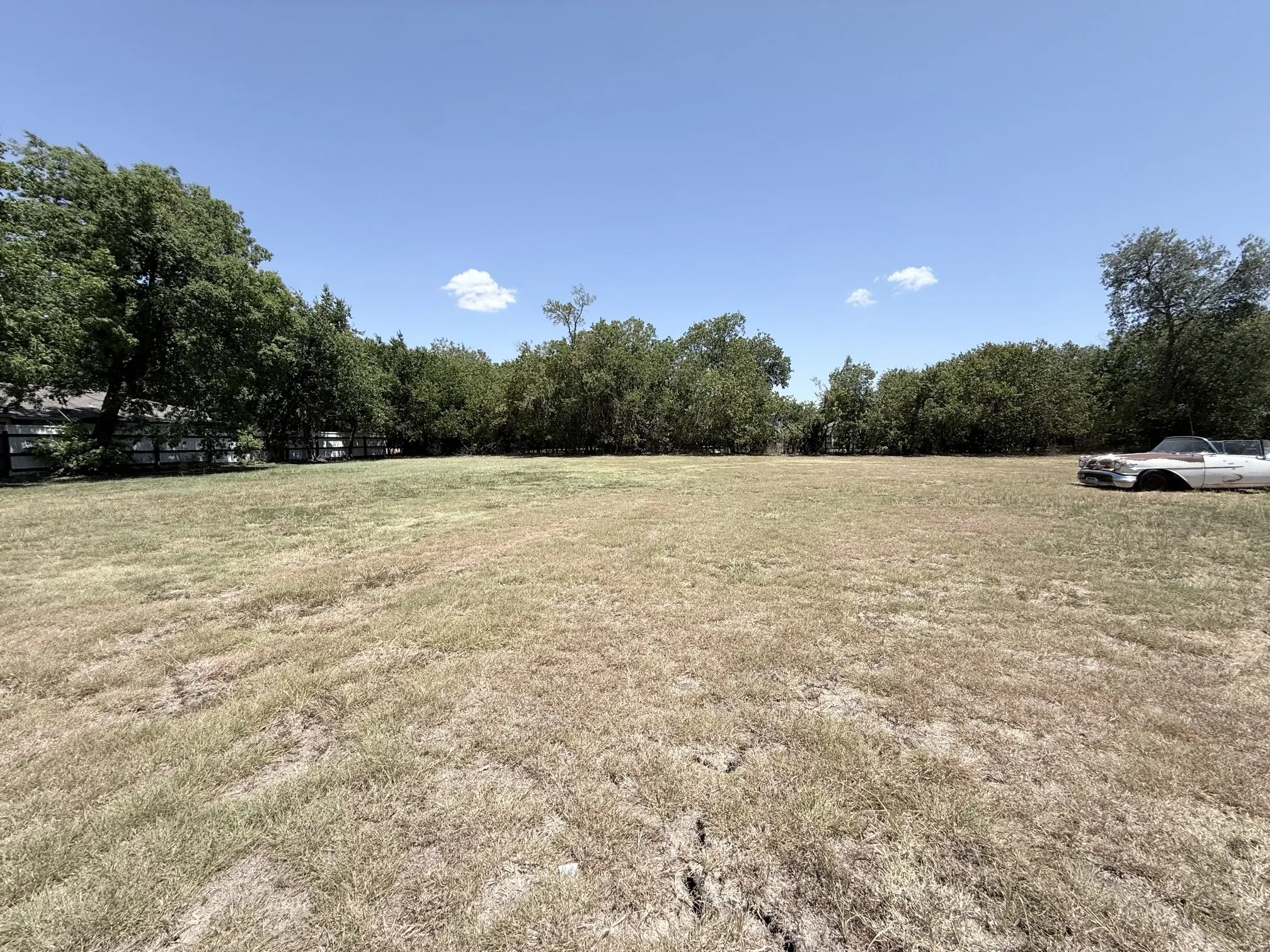 Expansive undeveloped lot with perimeter trees and a clear sky