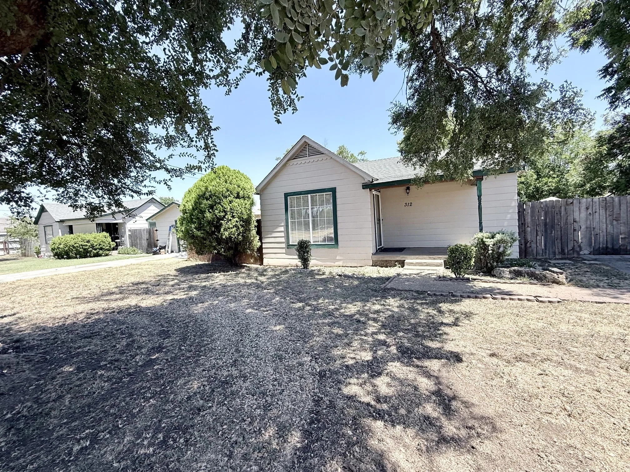Front yard with established trees, a fenced perimeter, and a concrete walkway