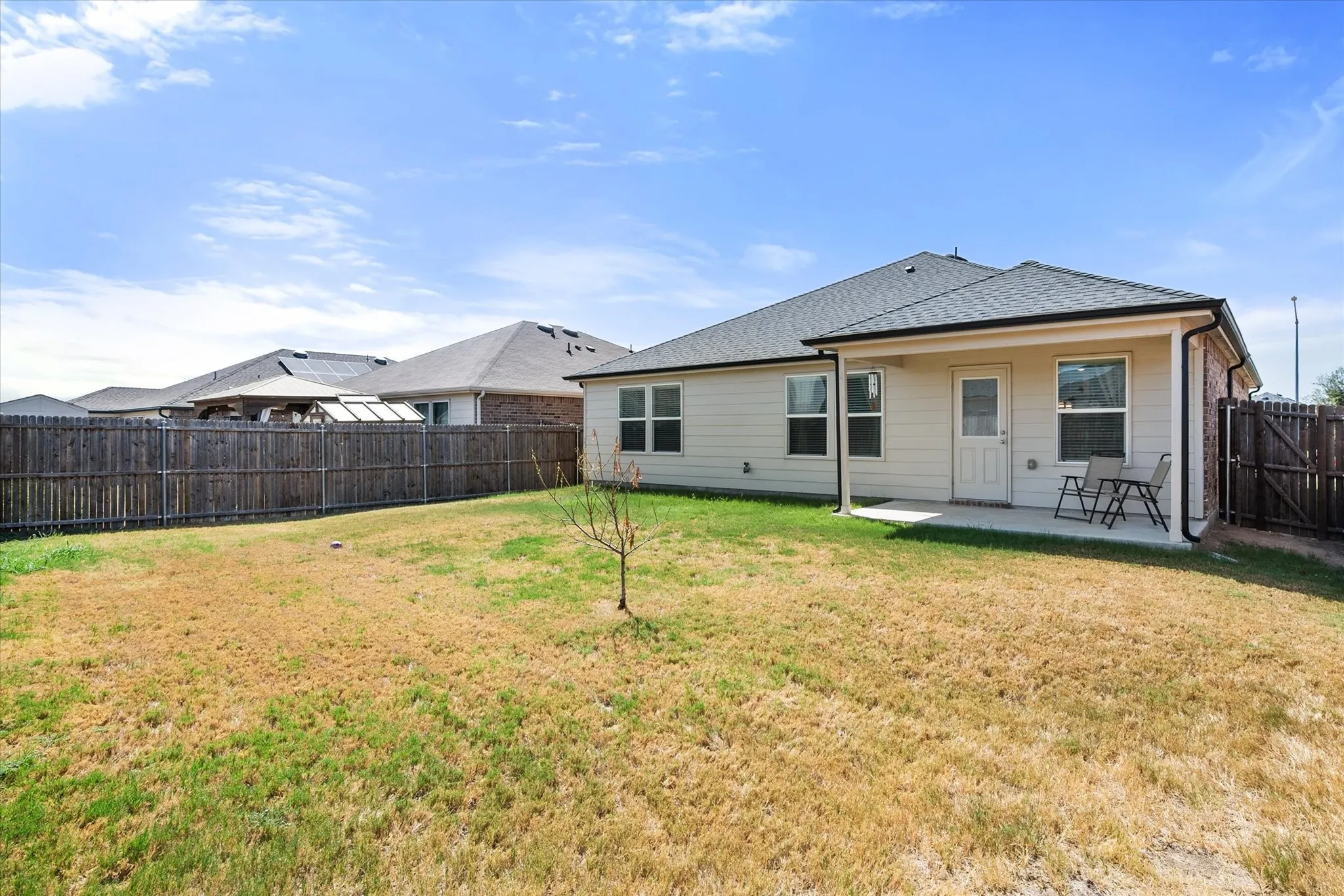 Expansive backyard featuring a wood privacy fence, covered concrete patio, and exterior siding