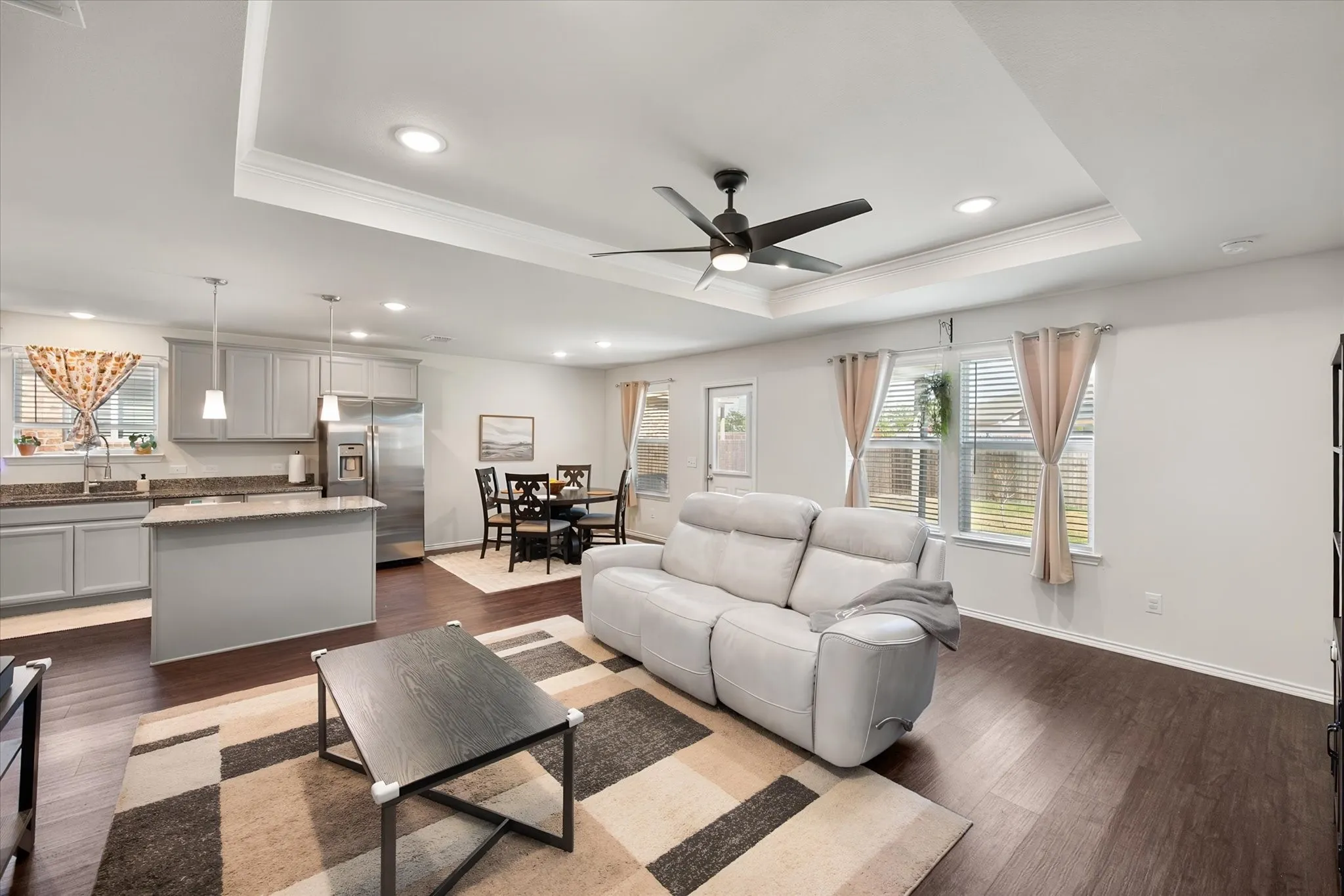 Tray ceiling with a ceiling fan, recessed lighting, wood-finish flooring, light gray kitchen cabinetry, and stainless steel appliances