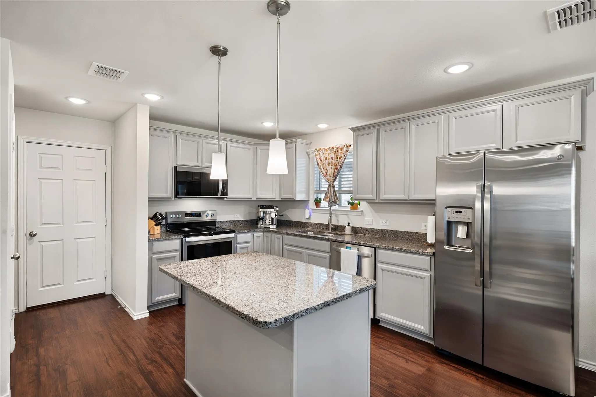 Kitchen featuring an island with stone countertop, stainless steel appliances, pendant lighting, recessed lighting, and wood-finish flooring