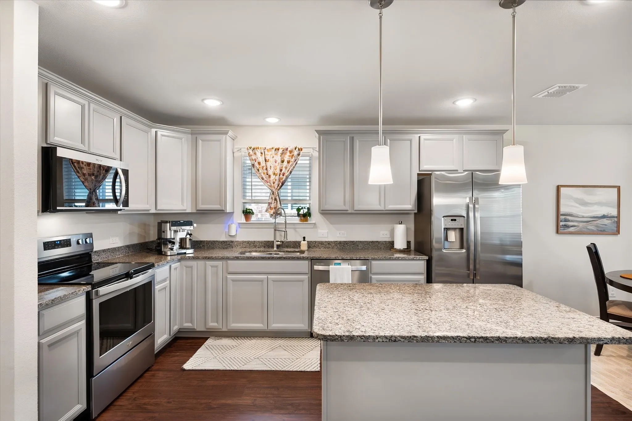 Kitchen featuring light-toned cabinetry, granite countertops, stainless steel appliances, and a central island with pendant lighting