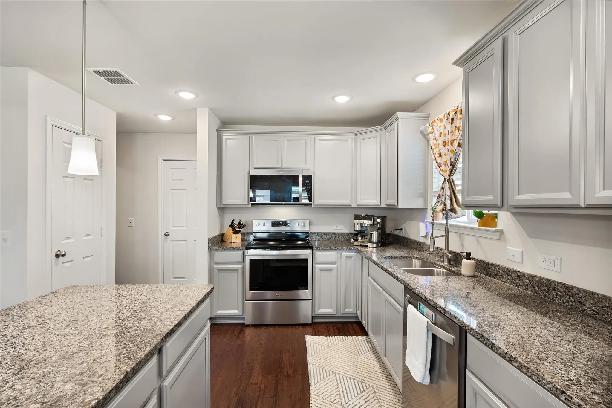Gray cabinetry with brushed nickel hardware, stainless steel appliances, speckled stone countertops, dark wood-finish flooring, and recessed lighting