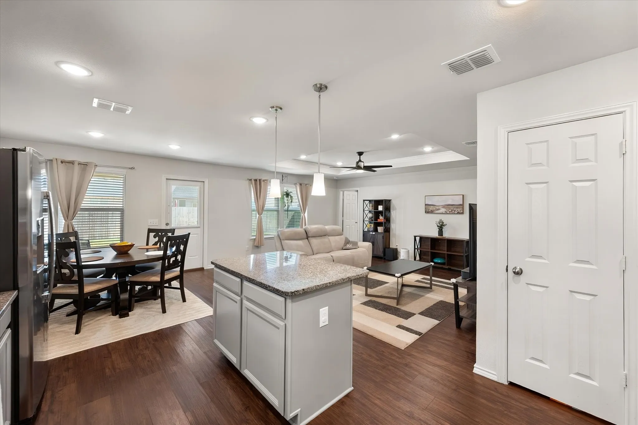 Open-concept living space featuring wood-finish flooring, recessed lighting, a kitchen island with a stone countertop, and a tray ceiling in the living area