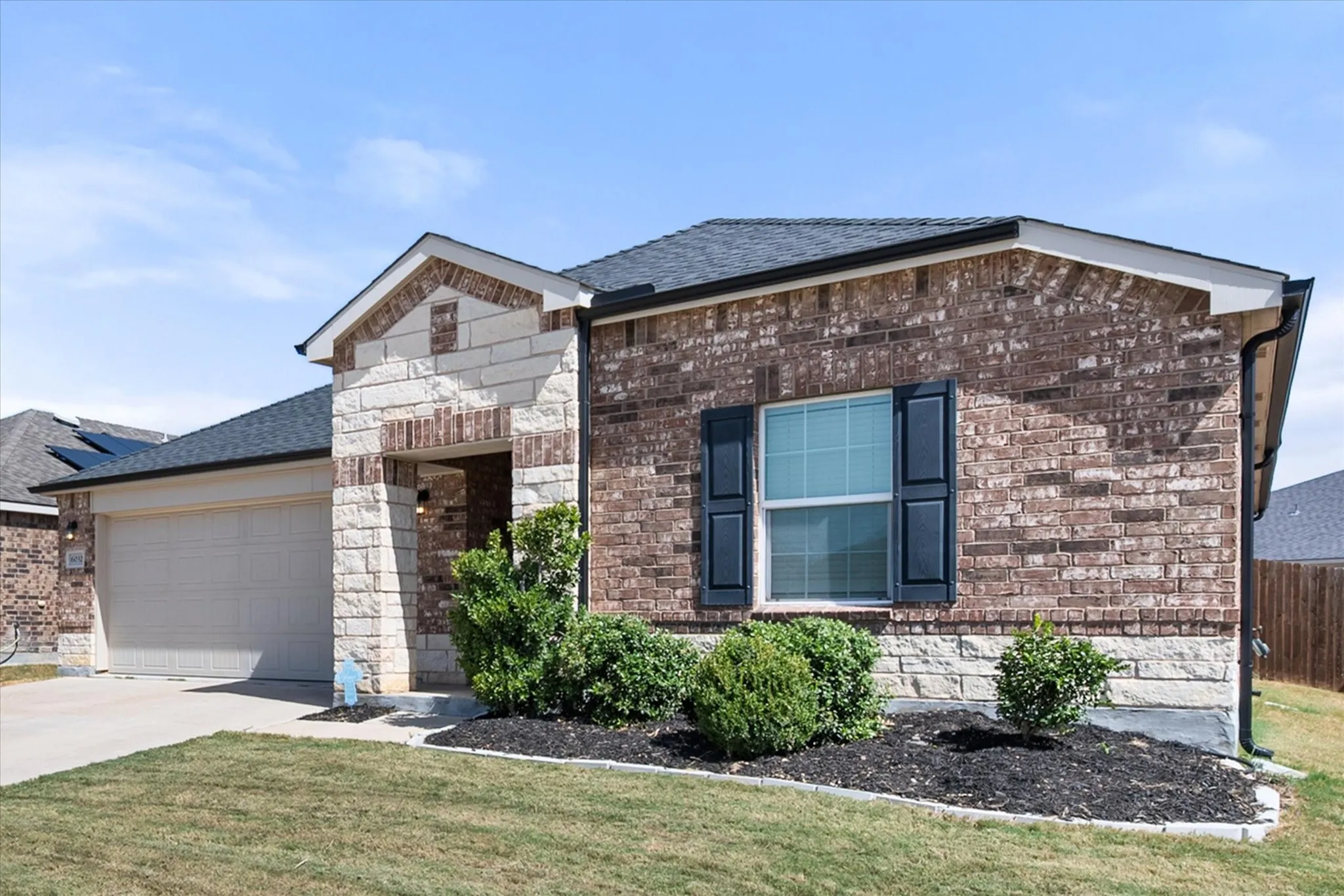 Brick and stone exterior with dark shutters, attached garage, and landscaping