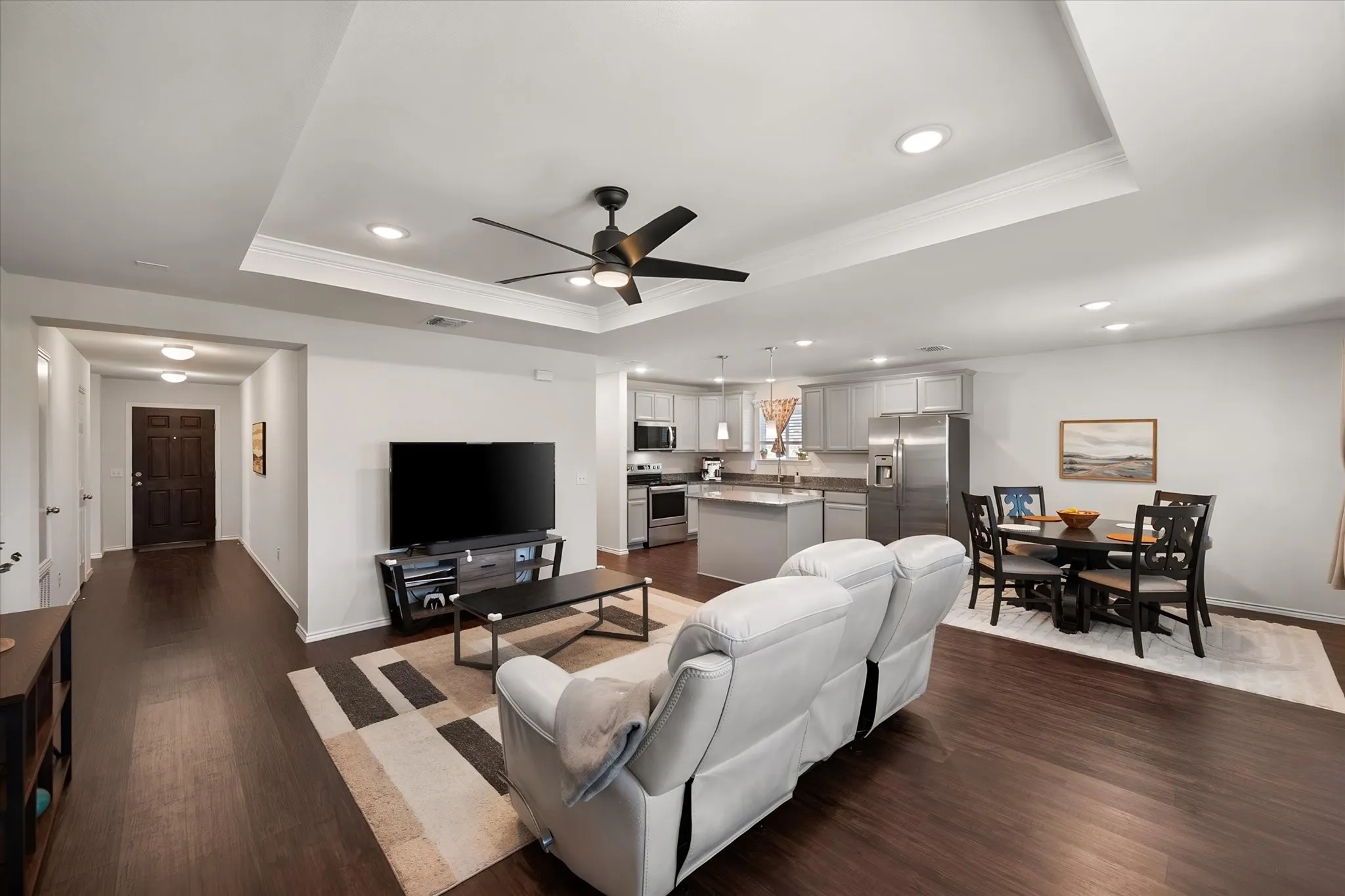 Open-concept living space with wood-finish flooring, recessed lighting, and a tray ceiling with a ceiling fan